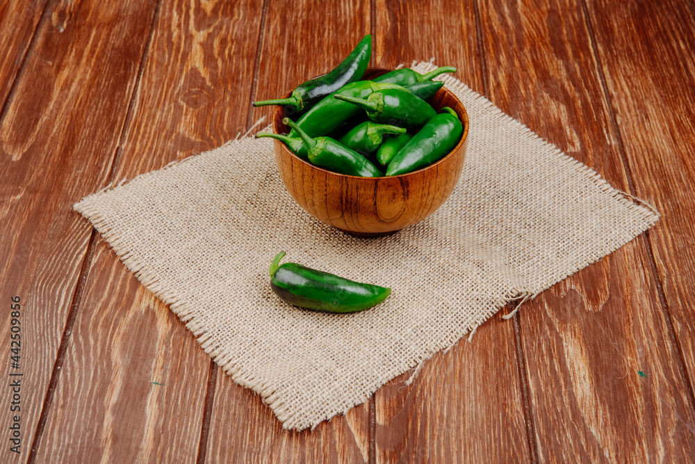 side view of fresh green chili peppers in a wooden bowl on sackcloth on rustic background side view of fresh green chili peppers in a wooden bowl on sackcloth on rustic background