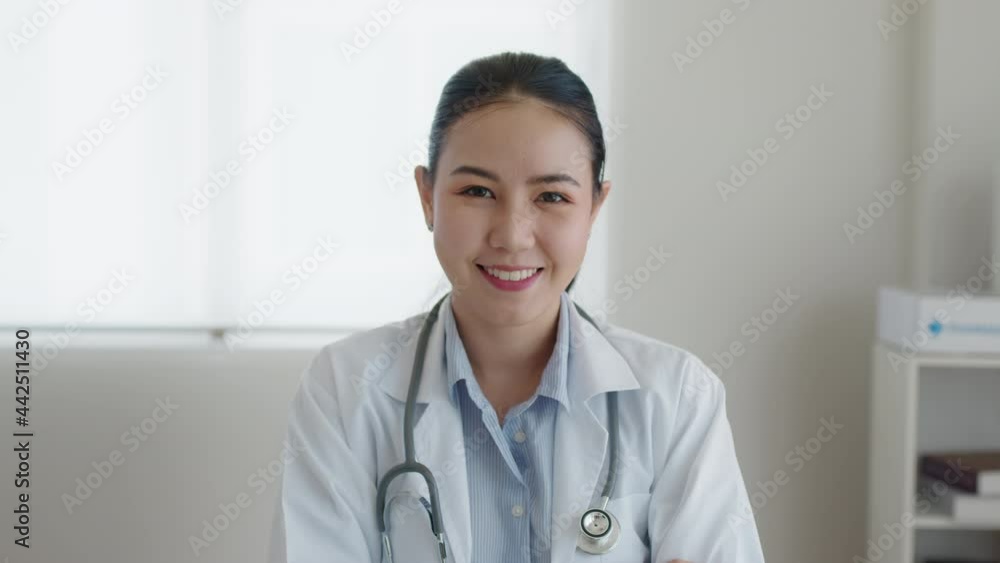 Young adult asia people or medic staff woman sitting toothy smile arm cross look at camera happy work on desk in clinic office room in telehealth telemedicine smart health care consult online service. Young adult asia people or medic staff woman sitting toothy smile arm cross look at camera happy work on desk in clinic office room in telehealth telemedicine smart health care consult online service.
