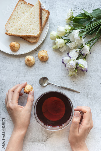 Top view of a woman's hands with a cup of tea, cookies, toasted bread and flowers