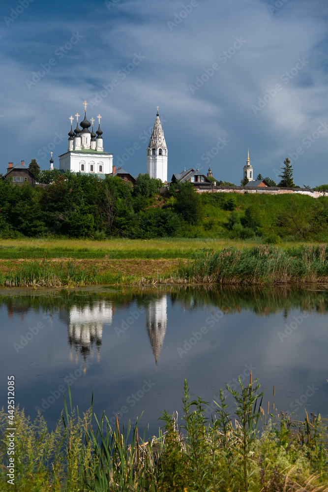 White buildings of ancient monastery in Suzdal, Russia, on bright sunny summer day, landscape, blue sky, reflection in water.