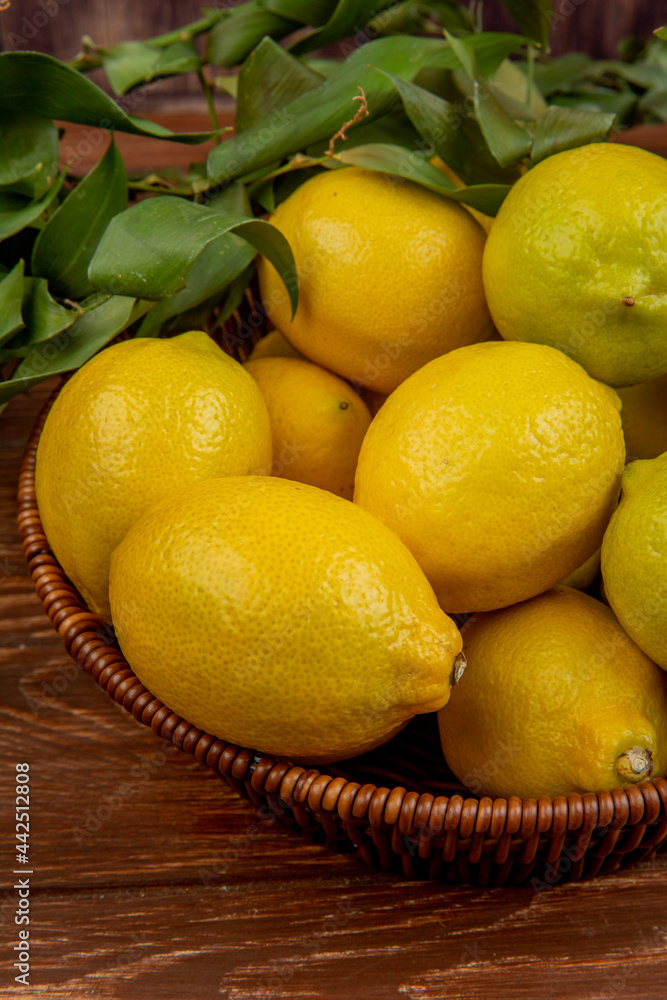 side view of fresh ripe lemons with green leaves in a wicker basket on on rustic wooden background