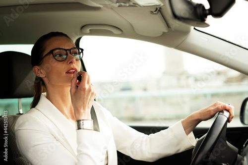 Beautiful young businesswoman sitting behind a wheel of a car doing make up. Attractive businesswoman preparing for the meeting...