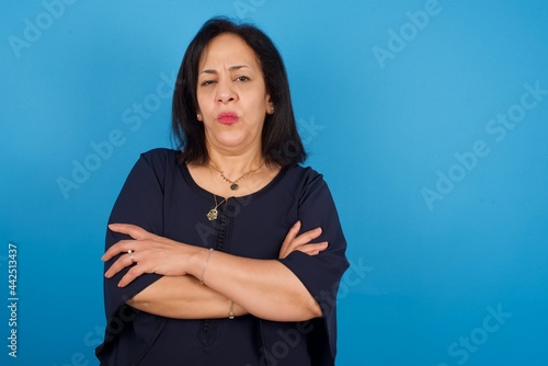 Fotografía Gloomy dissatisfied middle aged Arab woman standing against blue background look