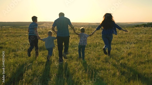 Happy family team, run together holding hands in park. Happy sons, children, mom and dad run, play, rejoice, enjoy nature in summer. Teamwork of people. A group of people of different ages at sunset.