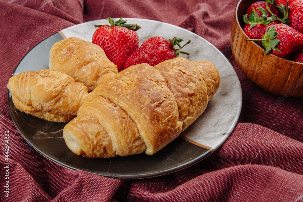 side view of fresh ripe strawberries with croissants on a plate on dark red fabric background side view of fresh ripe strawberries with croissants on a plate on dark red fabric background