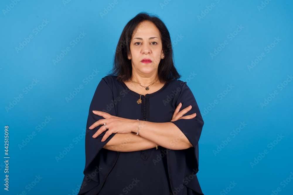 Picture of angry middle aged Arab woman standing against blue background looking camera. Picture of angry middle aged Arab woman standing against blue background looking camera.