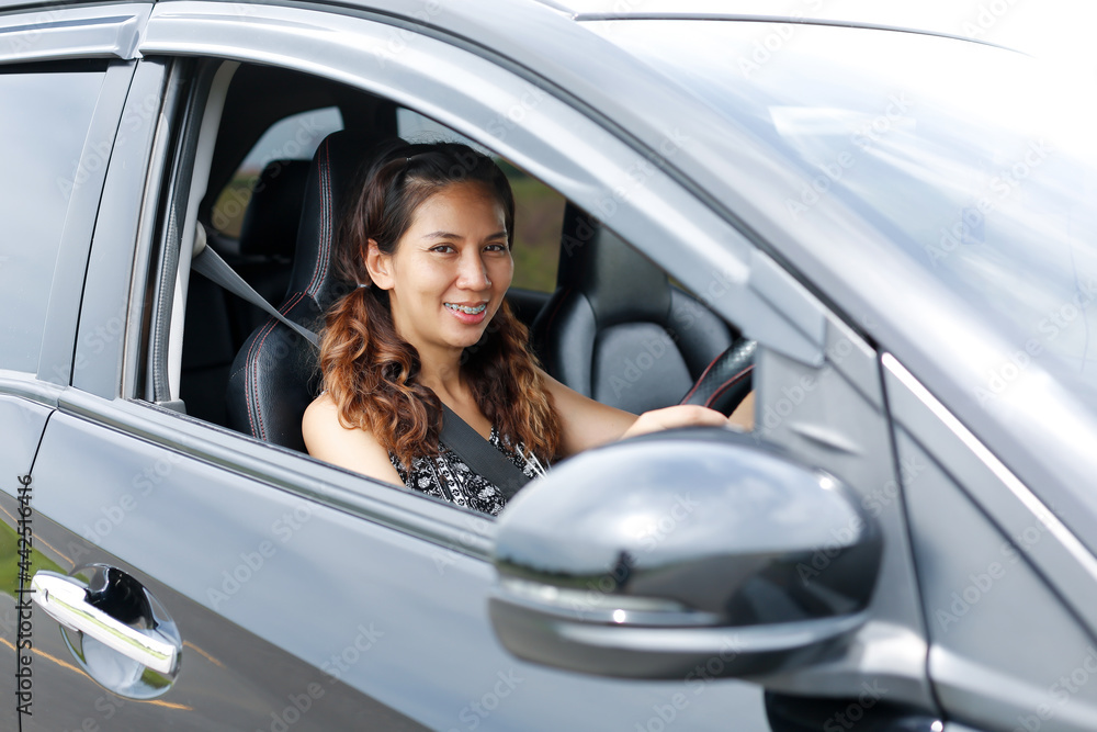 The happy woman driving a car and smiling. A cute young success happy brunette woman is driving a car. Portrait of happy female driver steering car with safety belt.