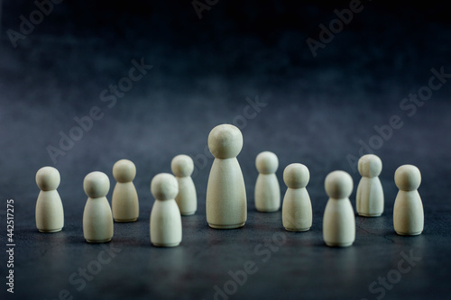 Wooden person model among small people on black background  Leadership concept.