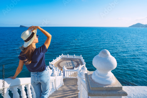 Young carefree tourist woman in white sun hat enjoying sea or ocean view in Balcon del Mediterraneo, Benidorm, Spain. Summer holiday vacation.