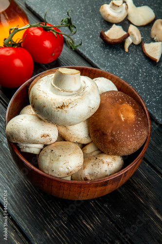 side view of of fresh mushrooms in a wooden bowl and fresh tomatoes on black background
