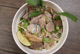 Vietnamese poh beef noodles soup broth with beef ball brisket tripe stomach parts been sprout thai basil lime in bowl on wooden table