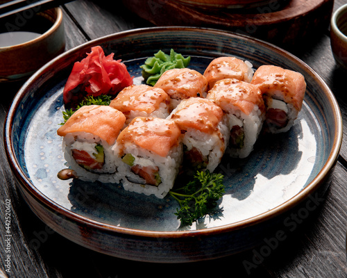 side view of sushi rolls with salmon and cream cheese served with ginger and wasabi on a plate on wooden background
