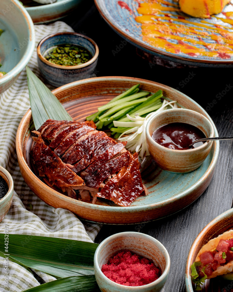 side view of traditional asian food peking duck with cucumbers and sauce on a plate