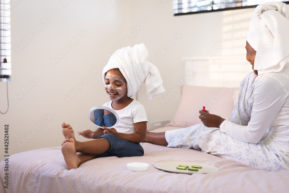 Happy african american mother and daughter relaxing in bedroom enjoying beauty treatments Happy african american mother and daughter relaxing in bedroom enjoying beauty treatments