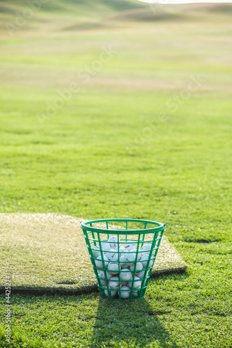 Green plastic basket with golf balls on the golf course at sunset