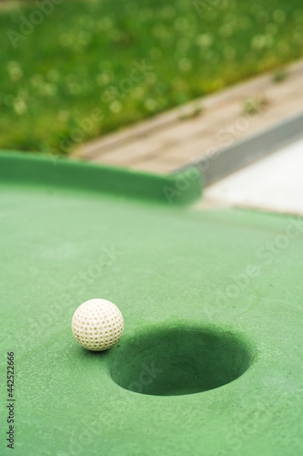 Mini golf. White ball near hole on green court. Summer outdoor game.