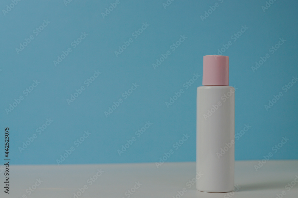 White jar of cream with a pink lid on a blue background, on a white table. With space for text on the left. Space for text on the left. Stylish appearance of the product, layout, identity. White jar of cream with a pink lid on a blue background, on a white table. With space for text on the left. Space for text on the left. Stylish appearance of the product, layout, identity.