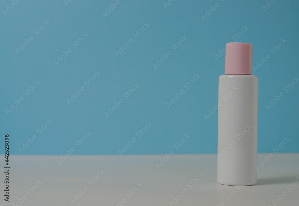 White jar of cream with a pink lid on a blue background, on a white table. With space for text on the left. Space for text on the left. Stylish appearance of the product, layout, identity. White jar of cream with a pink lid on a blue background, on a white table. With space for text on the left. Space for text on the left. Stylish appearance of the product, layout, identity.