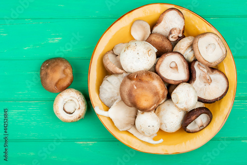 top view of fresh mushrooms on a yellow plate on green wooden background