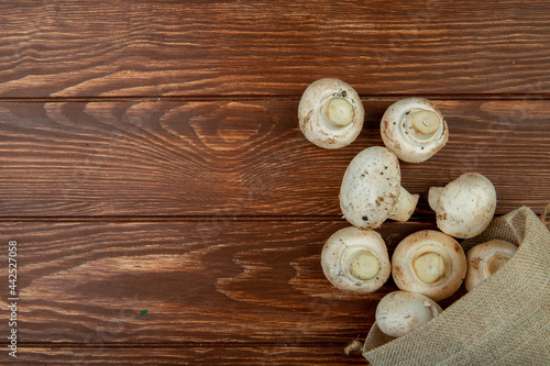 top view of fresh mushrooms scattered from a sack on rustic wooden background with copy space