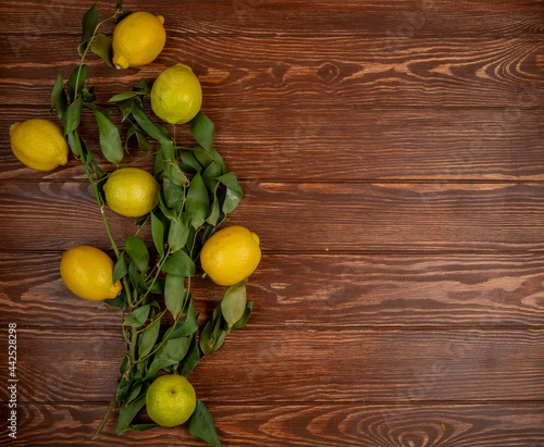 top view of fresh ripe lemons with green leaves on on rustic wooden background with copy space