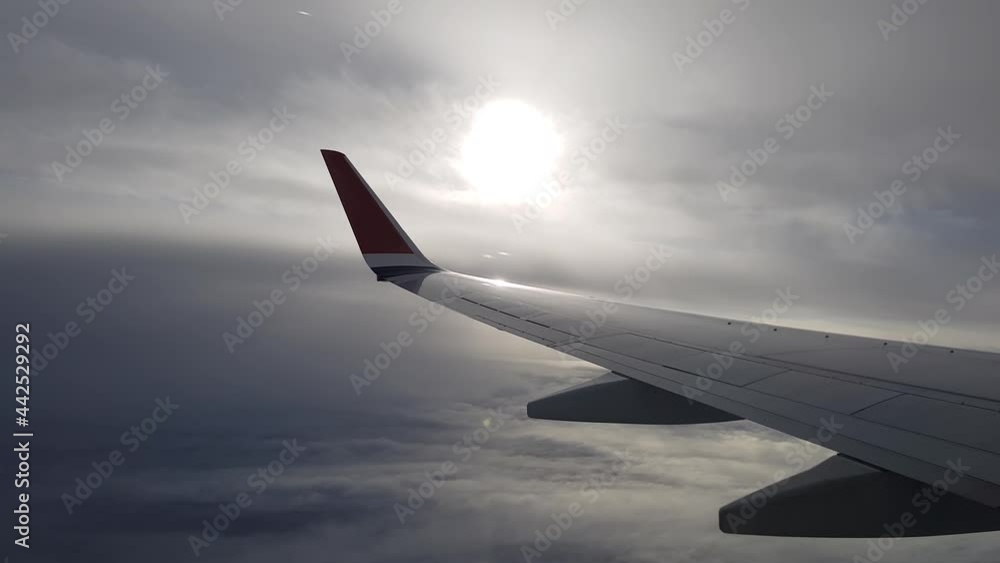 Airplane flight. Left wing of an airplane flying above the clouds with Sun behind clouds. View from the window of the plane. Airplane, Aircraft. Traveling by air Airplane flight. Left wing of an airplane flying above the clouds with Sun behind clouds. View from the window of the plane. Airplane, Aircraft. Traveling by air