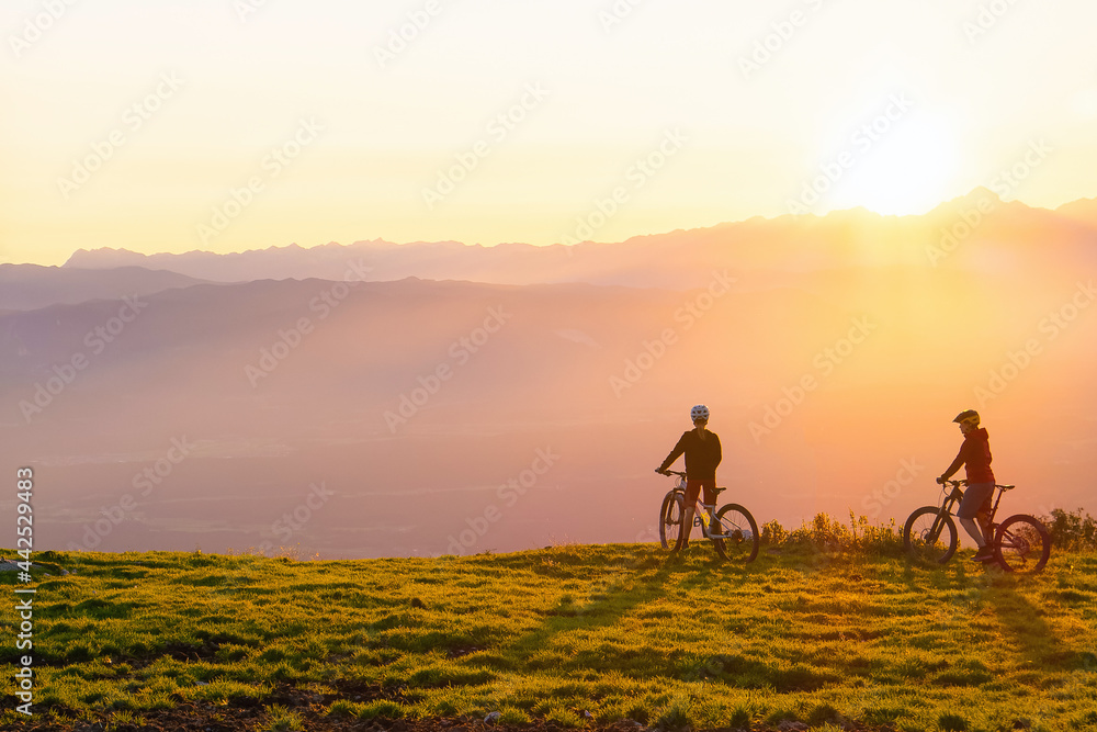 Fototapeta premium Mother and daughter cycling on mountain bikes at a sunset in mountains.