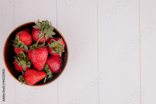 top view of fresh ripe strawberries in a wooden bowl on white background with copy space
