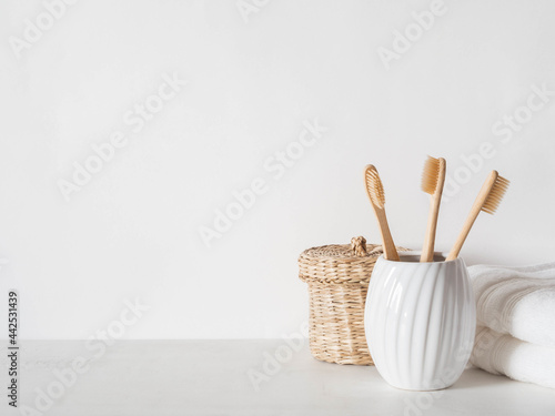 Minimal bath background with bamboo toothbrushs in ceramic glass, wicker box and white towels