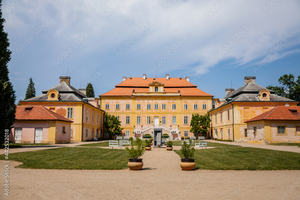 Krasny Dvur Chateau, North Bohemia, Czech Republic, 19 June 2021: Baroque yellow castle with stairs, front yard with green lawn and white benches at sunny summer day
