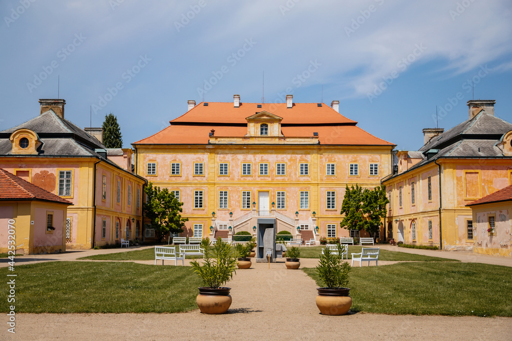 Krasny Dvur Chateau, North Bohemia, Czech Republic, 19 June 2021: Baroque yellow castle with stairs, front yard with green lawn and white benches at sunny summer day