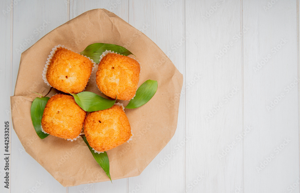 top view of muffins with green leaves on a craft brown paper on white rustic background with copy space top view of muffins with green leaves on a craft brown paper on white rustic background with copy space