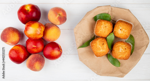 top view of muffins with green leaves on craft brown paper with fresh ripe nectarines on white rustic wooden background