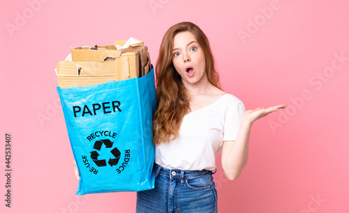 red head pretty woman looking surprised and shocked, with jaw dropped holding an object and holding a recycled paper bag photo