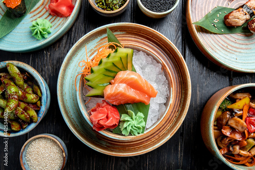 top view of salmon sashimi with sliced cucumbers  ginger and wasabi sauce on ice cubes in a bowl on wooden table