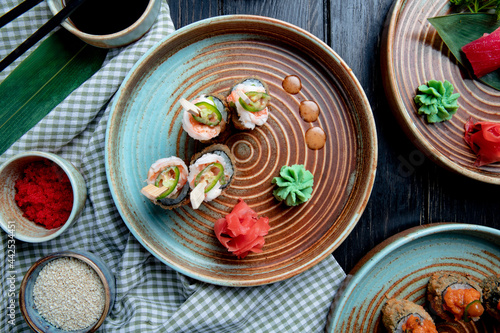 top view of set of baked sushi rolls with shrimps served with wasabi and ginger on a plate on wooden background