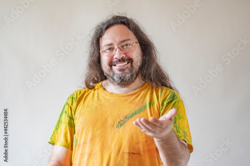 A blank with a man stretches out his empty hand forward. A casually and sloppy dressed man with a beard and long hair in a paint-stained T-shirt on a light background.