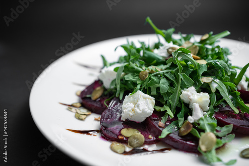 closeup of salad with beet, arugula and feta cheese on plate on black background