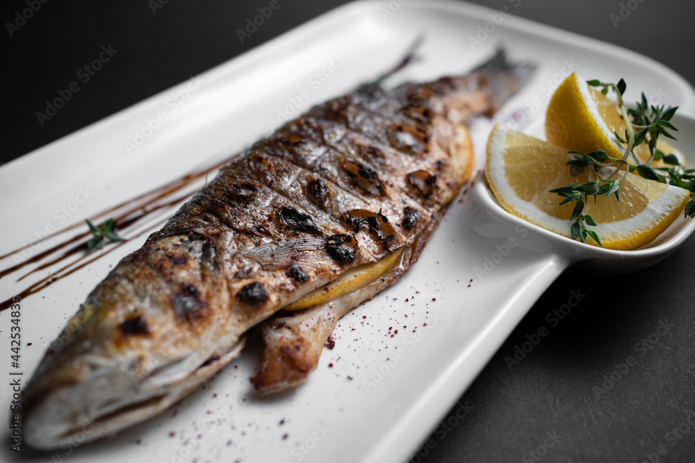 close up of whole grilled stuffed fish with lemon on plate on black background close up of whole grilled stuffed fish with lemon on plate on black background