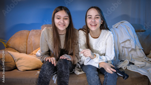 Two smiling girls sitting on sofa after playing video games on TV console at night
