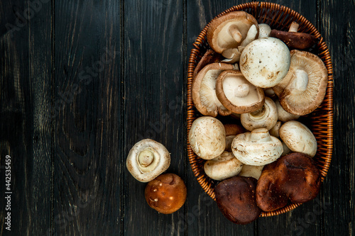 top view of various types of fresh mushrooms in a wicker basket on dark rustic wooden background with copy space