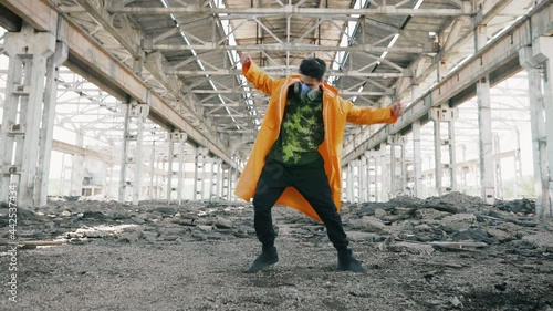 Young male dancer in protective mask performing various freestyle dance in ruined abandoned building