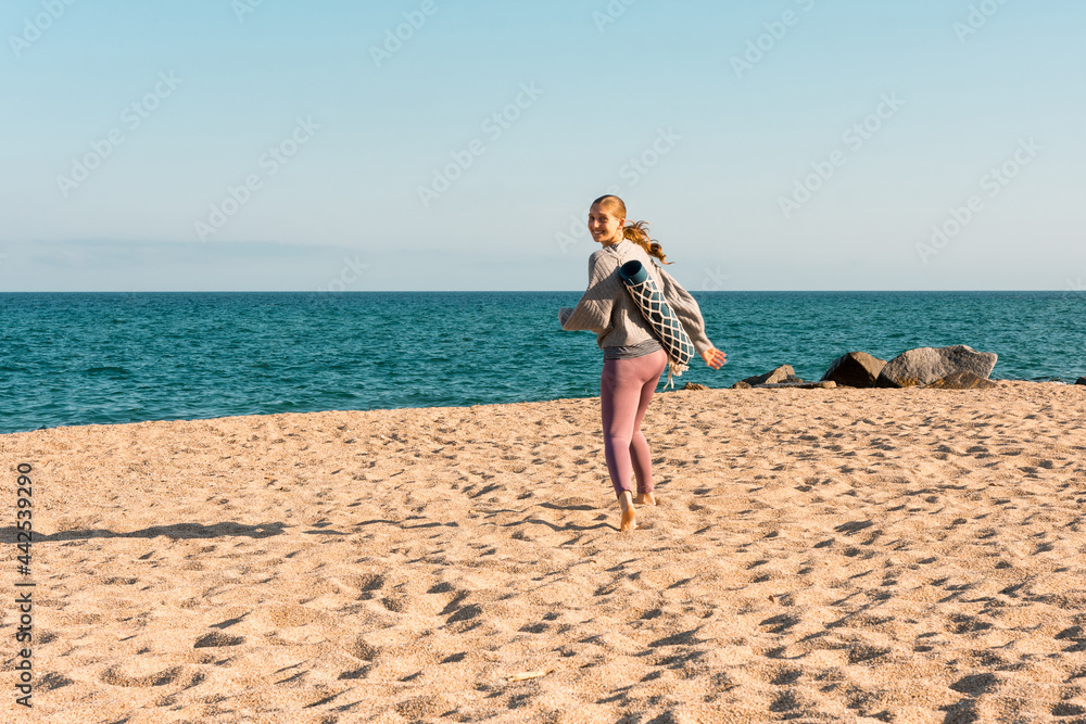 Fit woman with yoga mat standing on beach Fit woman with yoga mat standing on beach