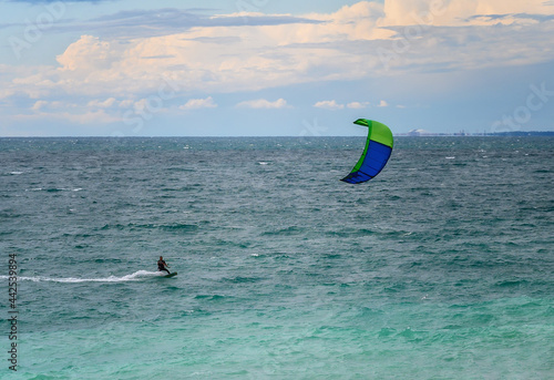 View of the sea coast on a summer evening. Cloudy sky with evening colors. Silhouette of a kitesurfer with a parachute on the background of the gentle turquoise sea. Extreme tourism in summer 