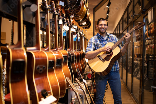 Talented caucasian musician testing new guitar instrument in music shop.