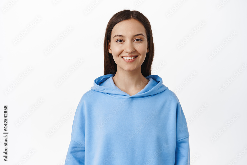 Portrait of young brunette 20s woman, wearing blue hoodie, smiling white teeth, looking happy, standing against white background Portrait of young brunette 20s woman, wearing blue hoodie, smiling white teeth, looking happy, standing against white background