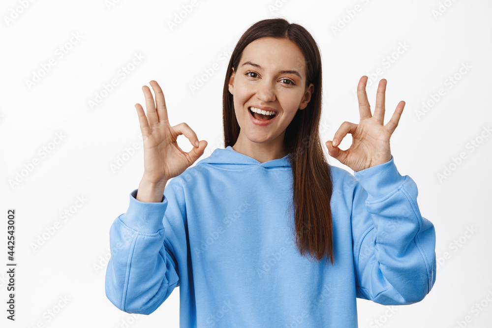 Not bad, congrats. Smiling brunette 20s woman, showing okay OK signs and looking satisfied, praise great choice, good work, give approval, complimenting, standing over white background Not bad, congrats. Smiling brunette 20s woman, showing okay OK signs and looking satisfied, praise great choice, good work, give approval, complimenting, standing over white background