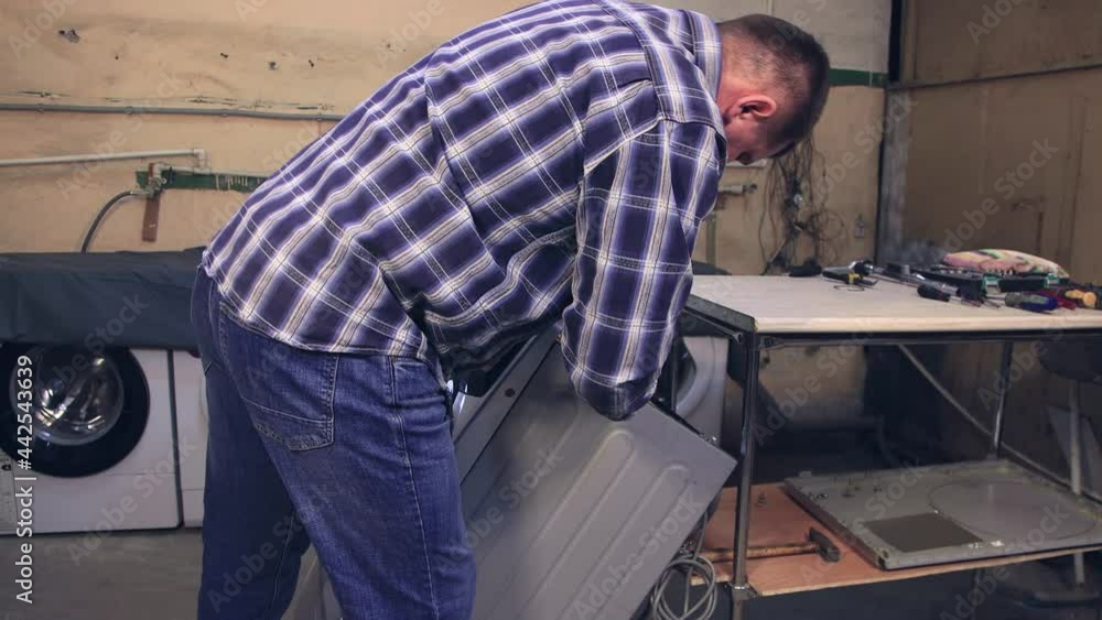 The wizard attaches the front panel with an electric screwdriver. The man disassembles, assembles, repairs the washing machine. Business concept in the field of maintenance and repair services. UHD 4K The wizard attaches the front panel with an electric screwdriver. The man disassembles, assembles, repairs the washing machine. Business concept in the field of maintenance and repair services. UHD 4K