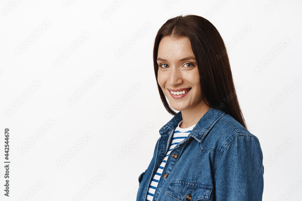 Close up of adult natural brunette with glowing, perfect skin, white smile, looking happy and confident at camera, standing half turned against white background Close up of adult natural brunette with glowing, perfect skin, white smile, looking happy and confident at camera, standing half turned against white background