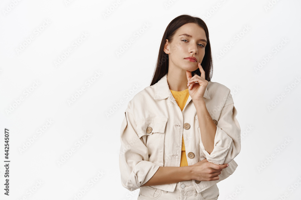 Thoughtful woman looking at camera, touch lip, thinking, making choice, deciding smth, standing in casual outfit against white background Thoughtful woman looking at camera, touch lip, thinking, making choice, deciding smth, standing in casual outfit against white background